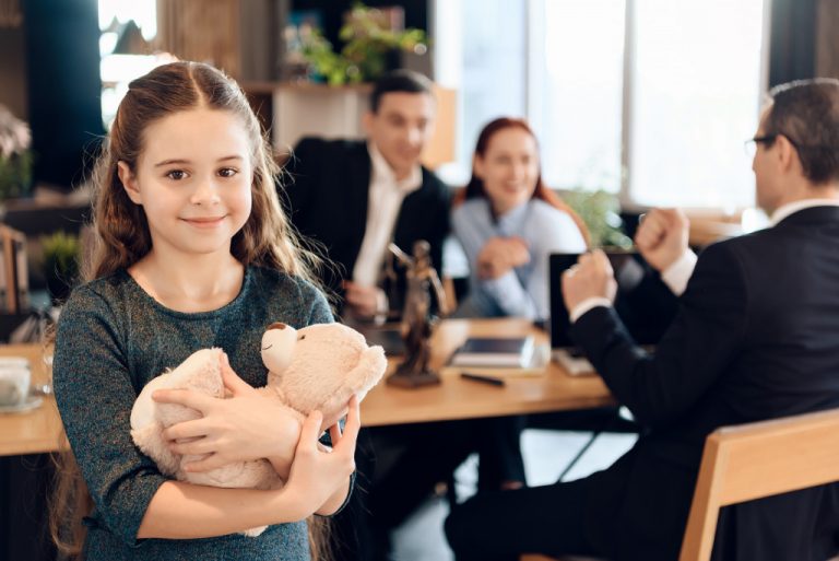 child happily hugging her teddy bear while her parent are discussing with the lawyer