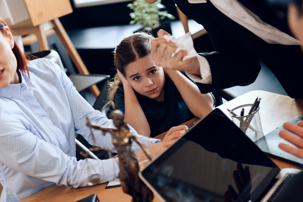 child covering her ears while parents and lawyer are having heated discussion