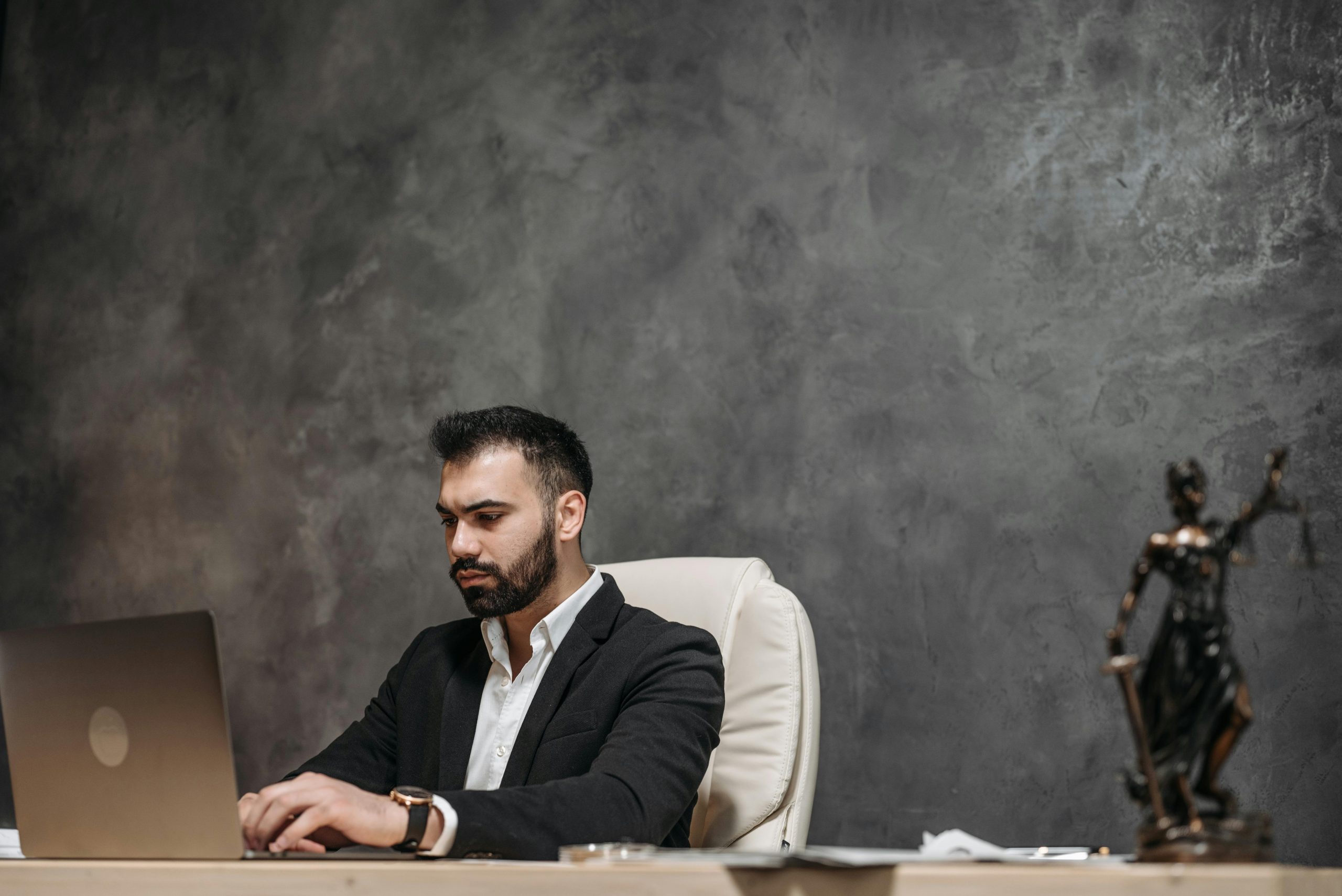 lady justice sculpture on a desk, with a lawyer using a laptop in the background